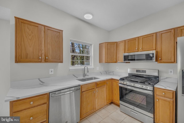 kitchen with light tile patterned floors, light stone countertops, appliances with stainless steel finishes, and a sink