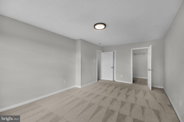 unfurnished bedroom with a textured ceiling, a closet, carpet flooring, baseboards, and a spacious closet