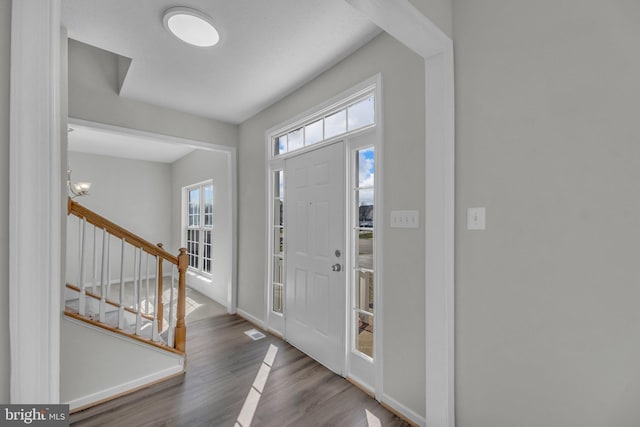 entrance foyer featuring visible vents, baseboards, wood finished floors, and stairs