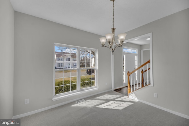 carpeted empty room with a notable chandelier, baseboards, visible vents, and a wealth of natural light