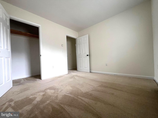 unfurnished bedroom with light carpet, a closet, and baseboards