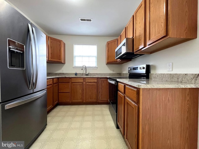 kitchen with visible vents, stainless steel appliances, brown cabinetry, light countertops, and light floors