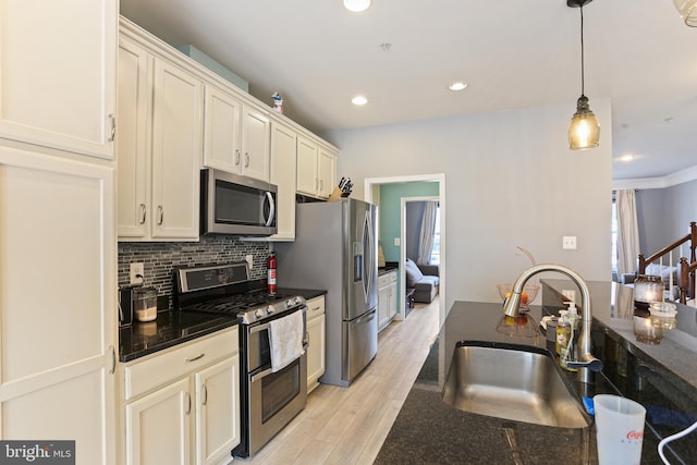 kitchen with light wood finished floors, decorative light fixtures, decorative backsplash, appliances with stainless steel finishes, and a sink