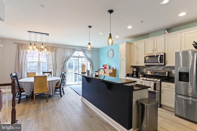 kitchen with dark countertops, tasteful backsplash, a center island with sink, light wood-style floors, and stainless steel appliances