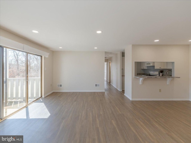 unfurnished living room featuring visible vents, baseboards, and wood finished floors