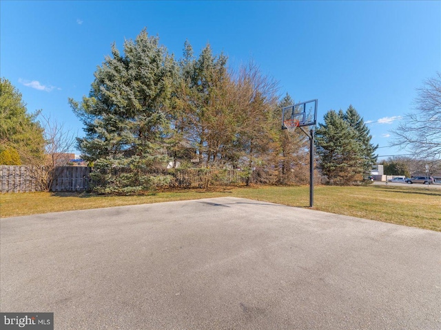 view of sport court with basketball hoop, fence, and a yard