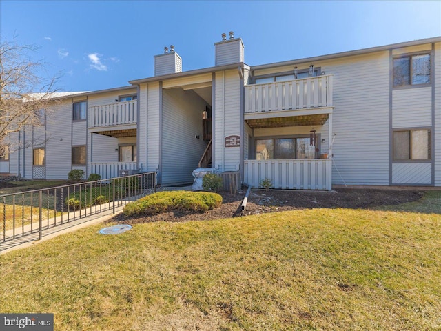 view of front of house featuring a front lawn, a chimney, fence, and a balcony