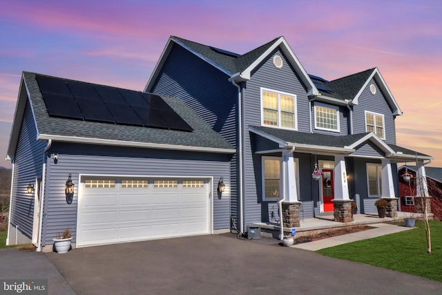 view of front facade with aphalt driveway, an attached garage, roof mounted solar panels, and a shingled roof