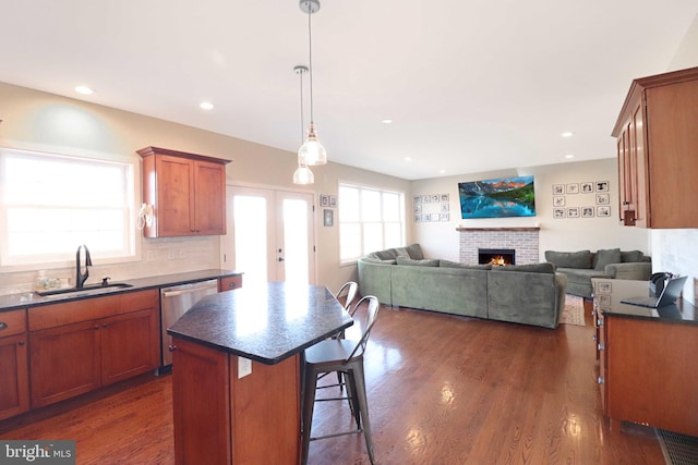 kitchen with a sink, dark countertops, stainless steel dishwasher, and a warm lit fireplace