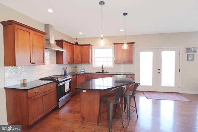 kitchen featuring stainless steel gas range oven, a breakfast bar, a sink, brown cabinetry, and wall chimney range hood