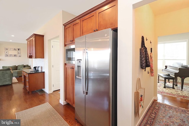 kitchen featuring dark wood-style flooring, appliances with stainless steel finishes, open floor plan, and brown cabinetry