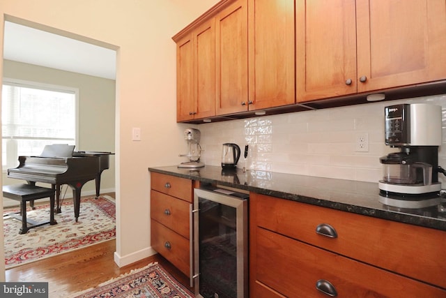 kitchen featuring wood finished floors, brown cabinets, dark stone counters, wine cooler, and tasteful backsplash