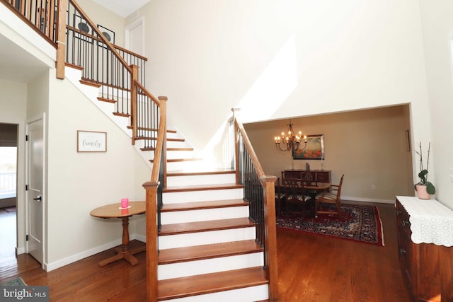 staircase featuring a high ceiling, wood finished floors, baseboards, and a chandelier