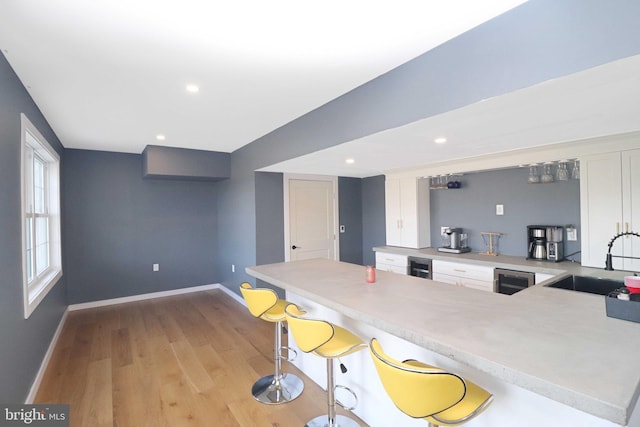 kitchen featuring light wood-type flooring, a sink, white cabinetry, a peninsula, and light countertops