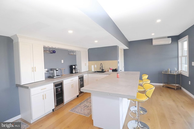 kitchen with a wall unit AC, beverage cooler, a breakfast bar, a peninsula, and white cabinets