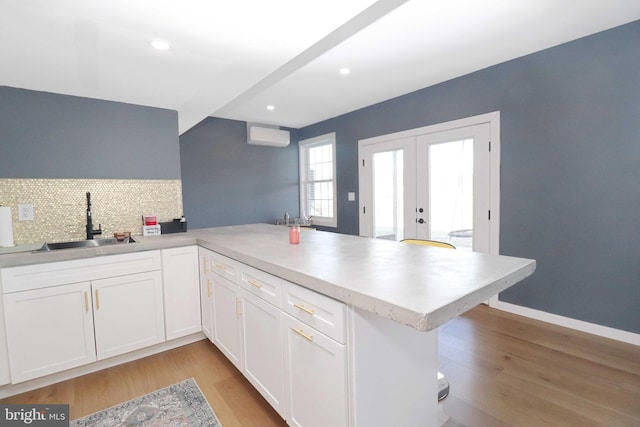 kitchen featuring light wood-type flooring, a sink, white cabinetry, french doors, and a peninsula