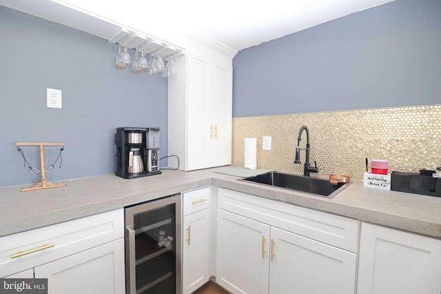 kitchen with beverage cooler, light countertops, decorative backsplash, white cabinets, and a sink