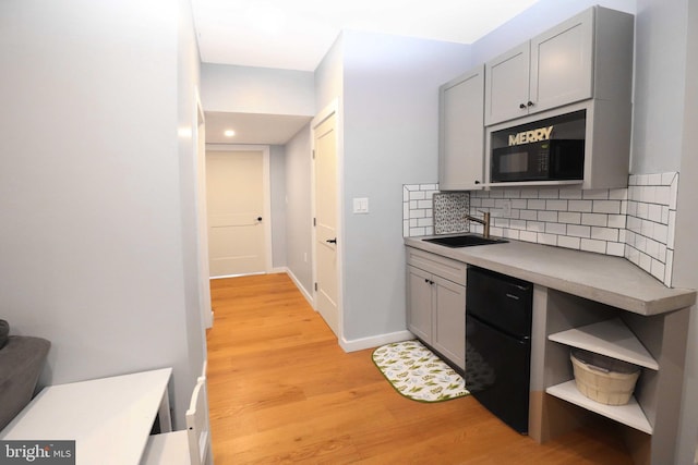 kitchen featuring tasteful backsplash, gray cabinetry, black microwave, light wood-style floors, and a sink