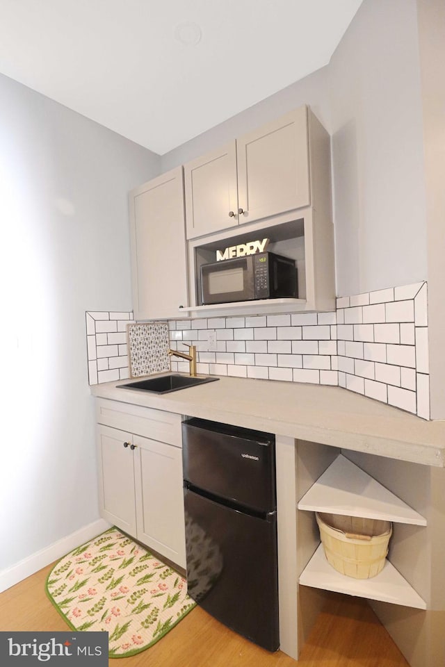 kitchen featuring a sink, backsplash, black appliances, and light countertops