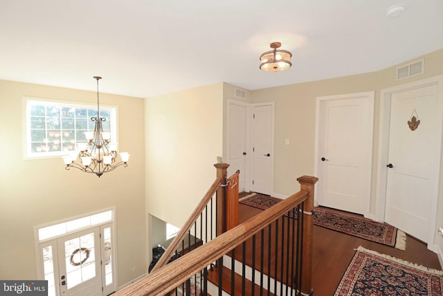 hall with an upstairs landing, visible vents, a notable chandelier, and wood finished floors