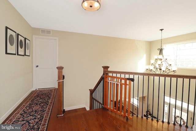 corridor featuring visible vents, an upstairs landing, wood finished floors, an inviting chandelier, and baseboards