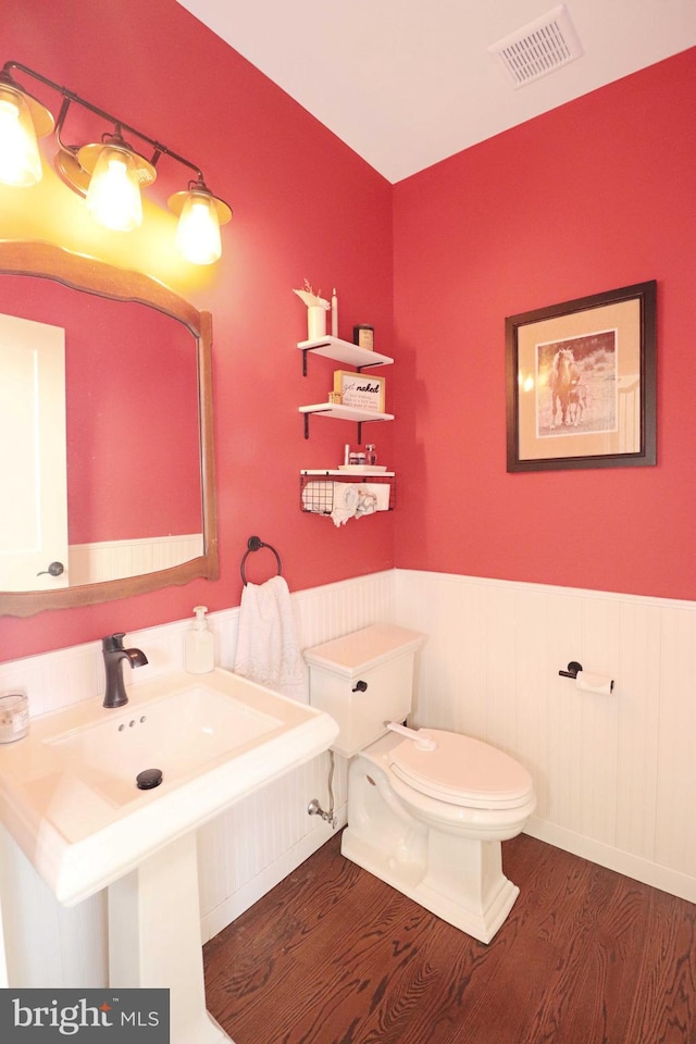 bathroom with visible vents, toilet, a sink, wood finished floors, and wainscoting