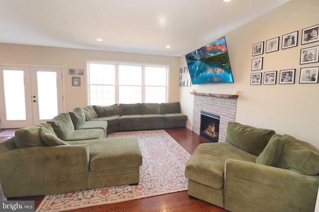 living room with dark wood finished floors, recessed lighting, a brick fireplace, and french doors