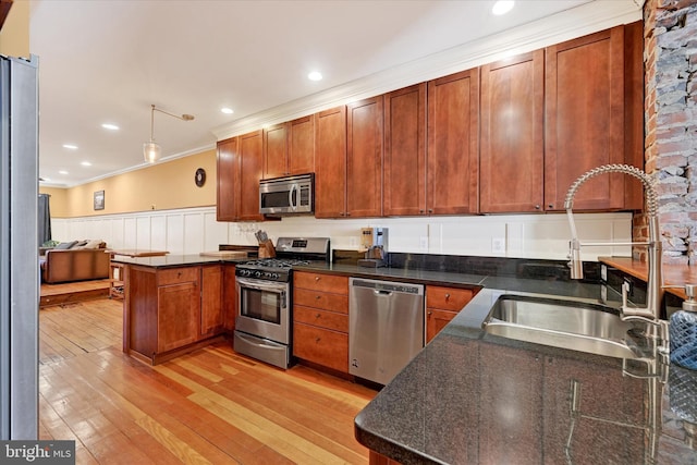 kitchen featuring a peninsula, light wood-style flooring, a sink, ornamental molding, and stainless steel appliances