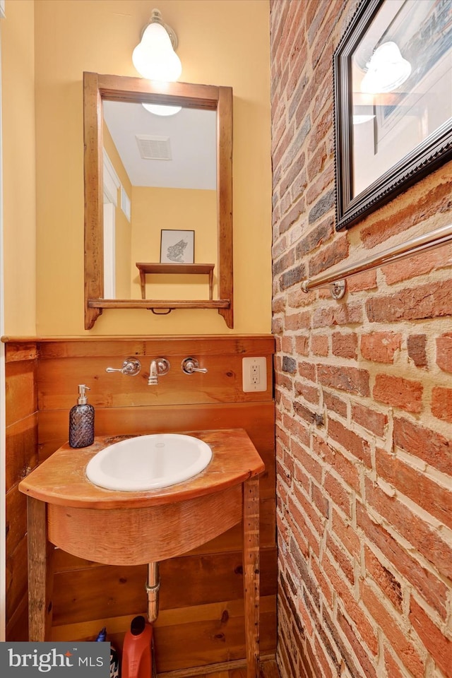 bathroom featuring visible vents, brick wall, a wainscoted wall, and a sink