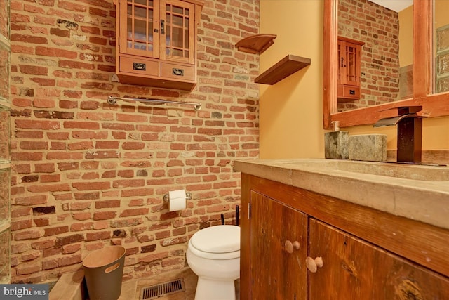 bathroom featuring vanity, toilet, visible vents, and brick wall