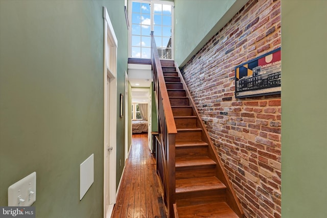 staircase featuring brick wall, a high ceiling, and hardwood / wood-style floors