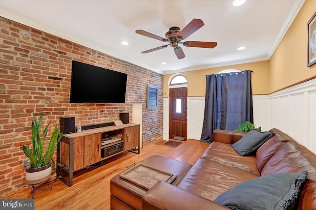 living area with a ceiling fan, brick wall, light wood-style flooring, ornamental molding, and wainscoting