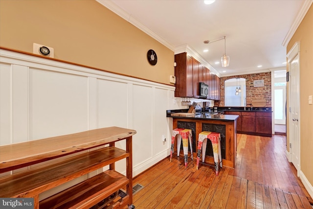 kitchen featuring dark countertops, stainless steel microwave, crown molding, light wood-type flooring, and a peninsula