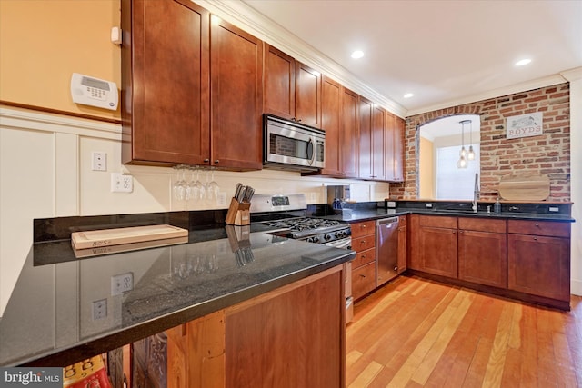 kitchen with pendant lighting, light wood-style flooring, appliances with stainless steel finishes, a peninsula, and a sink