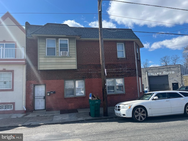 townhome / multi-family property with roof with shingles and brick siding