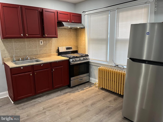 kitchen with tasteful backsplash, radiator, stainless steel appliances, under cabinet range hood, and a sink