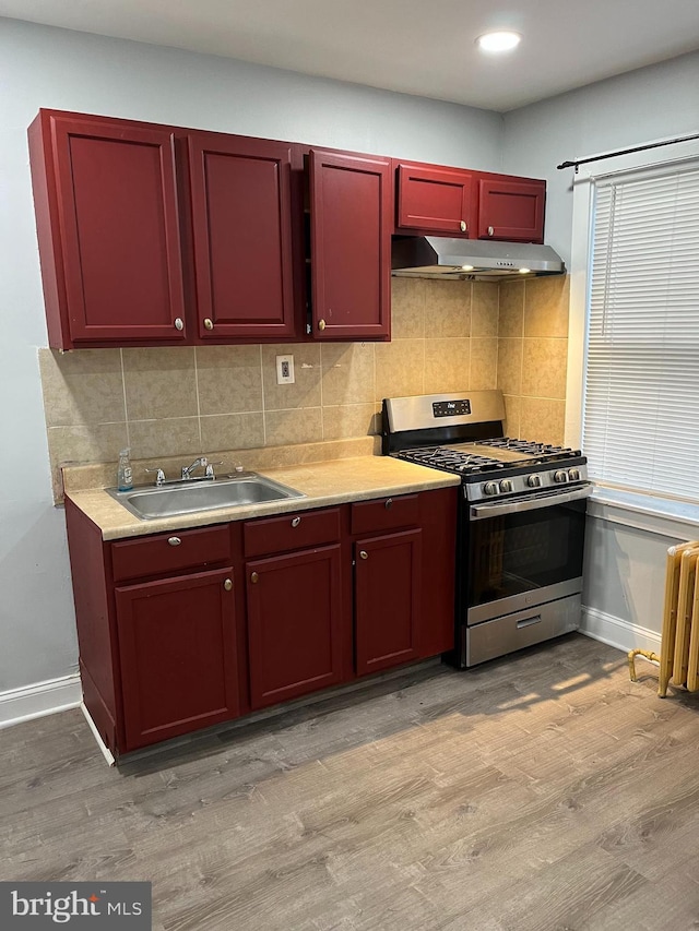 kitchen with under cabinet range hood, a sink, light wood-type flooring, radiator, and stainless steel gas stove