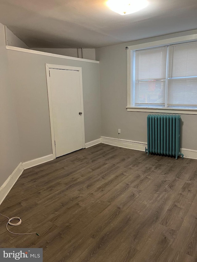 spare room featuring radiator, baseboards, and dark wood-style flooring