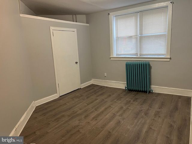 unfurnished room featuring baseboards, dark wood finished floors, and radiator heating unit