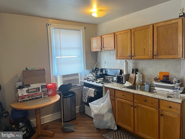 kitchen featuring decorative backsplash, brown cabinetry, dark wood-type flooring, gas range oven, and a sink