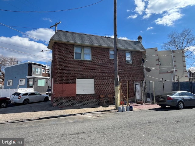 exterior space with brick siding, roof with shingles, and fence