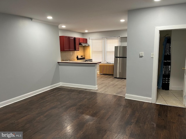 kitchen with radiator heating unit, appliances with stainless steel finishes, wood finished floors, dark brown cabinets, and under cabinet range hood