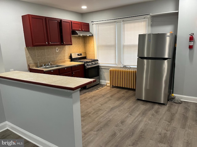 kitchen featuring stainless steel appliances, radiator, a sink, wood finished floors, and under cabinet range hood