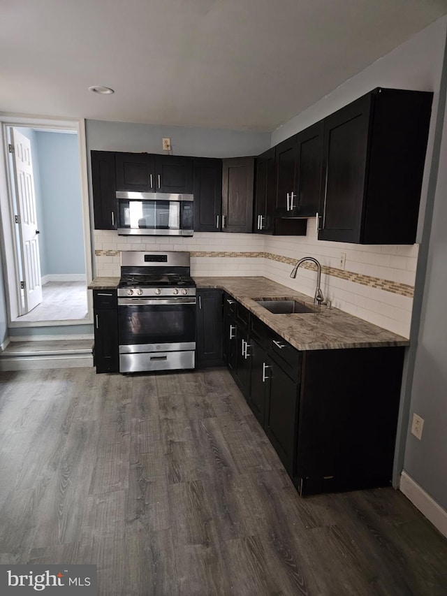 kitchen with dark wood-style floors, appliances with stainless steel finishes, a sink, and light stone countertops