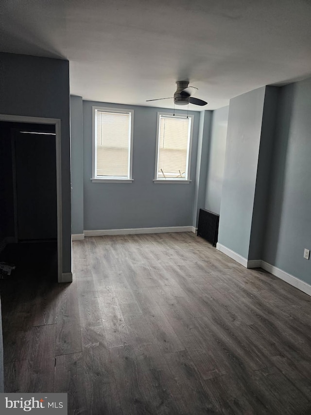 unfurnished bedroom featuring baseboards, ceiling fan, radiator heating unit, and wood finished floors