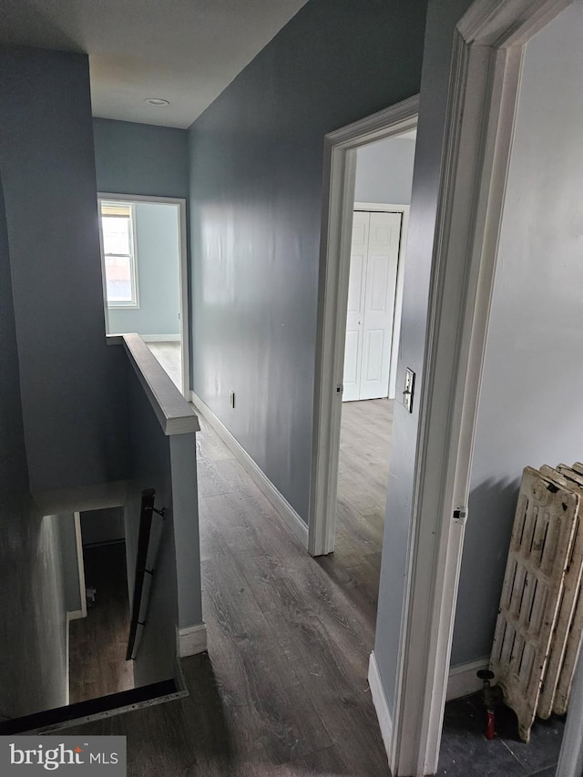 corridor with dark wood-style flooring, radiator heating unit, an upstairs landing, and baseboards