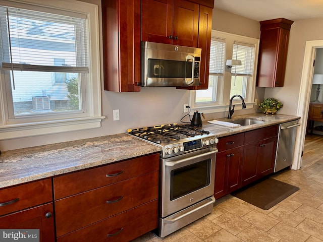 kitchen with appliances with stainless steel finishes, reddish brown cabinets, a sink, and light stone countertops