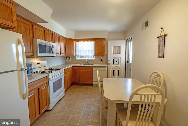 kitchen featuring visible vents, light countertops, brown cabinetry, white appliances, and a sink