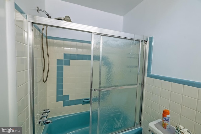 full bathroom with enclosed tub / shower combo, toilet, and tile walls