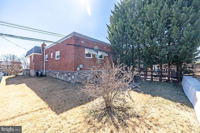 view of side of property with central AC unit, fence, and brick siding